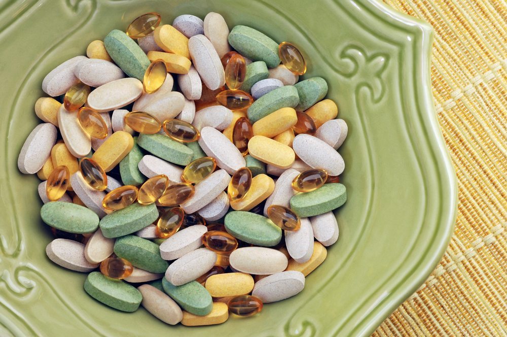 top view of a green bowl of various colourful pills on straw placemat