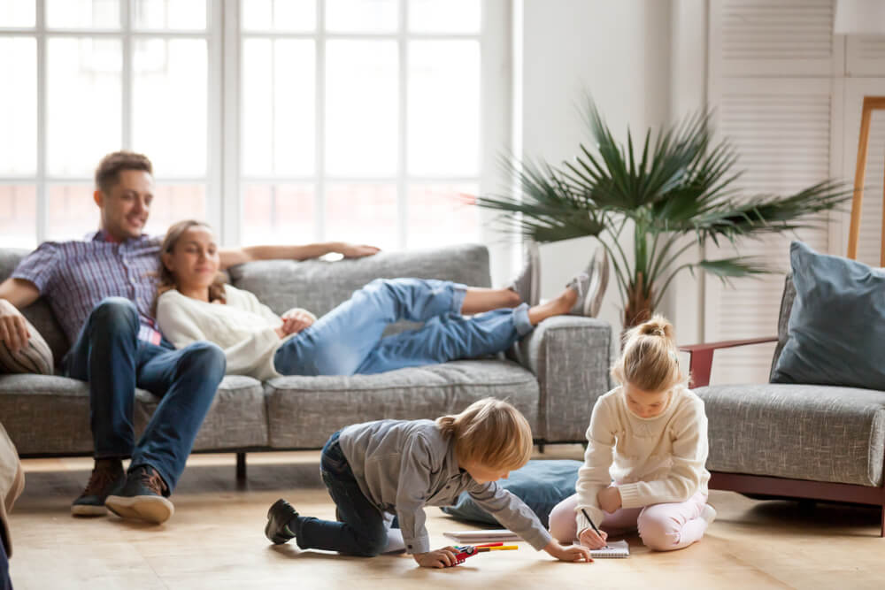 Happy parents and kids having fun tickling sitting together on sofa, cheerful couple laughing playing game with little active children son and daughter in living room at home, family funny activity