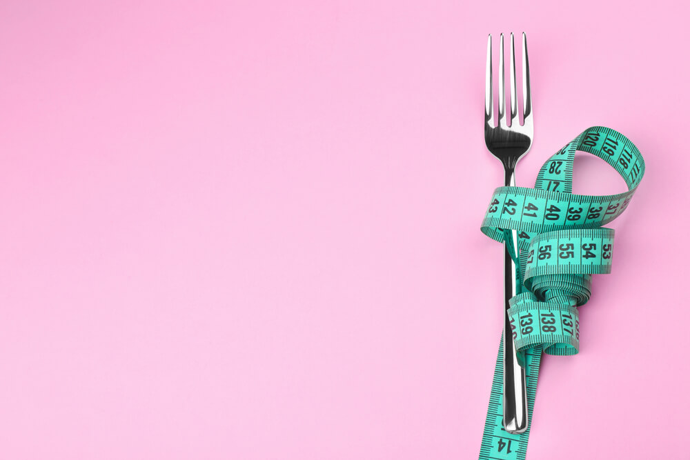 Measuring tape wrapped around fork lying on color surface