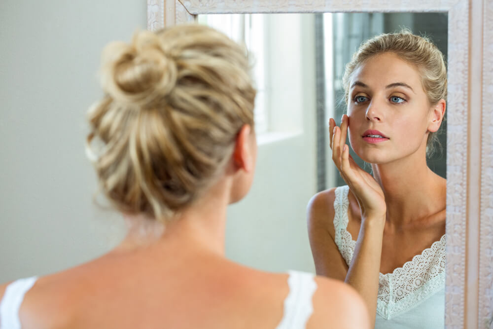 woman checking her skin in bathroom mirror