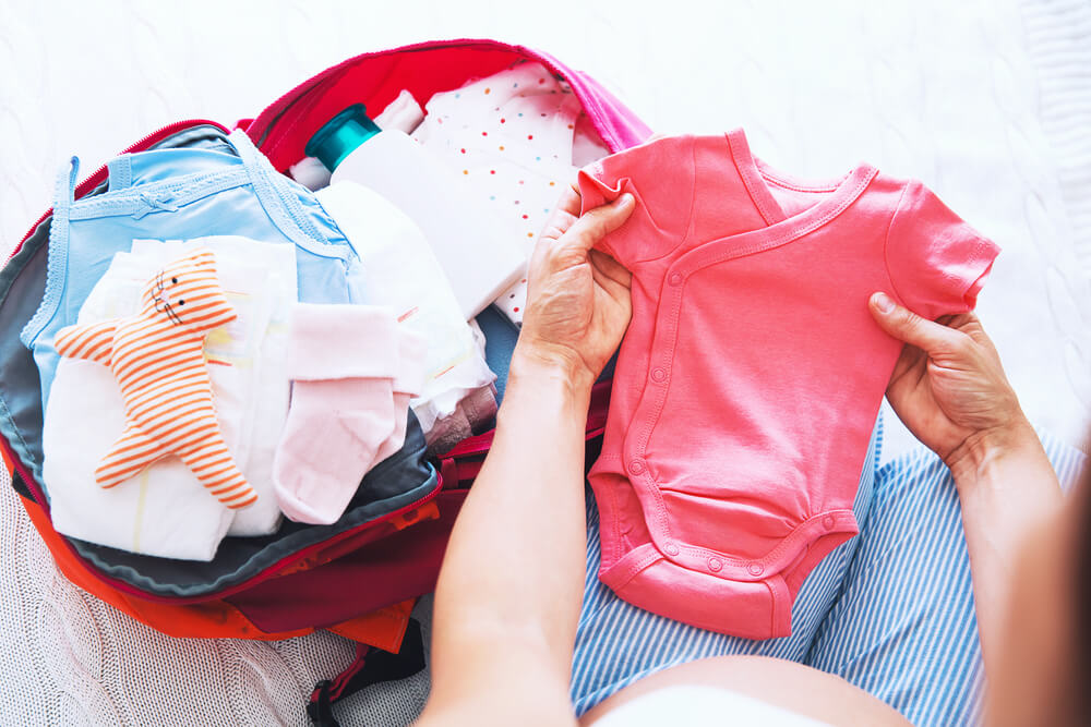Woman putting pink onesie into a suitcase