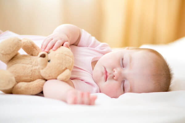 baby in pink onesie sleeping and holding teddy bear