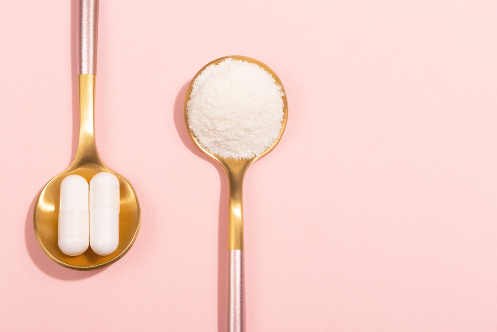 two gold spoons on a light pink background. In one spoon there's two white pills, in another it's white powder.