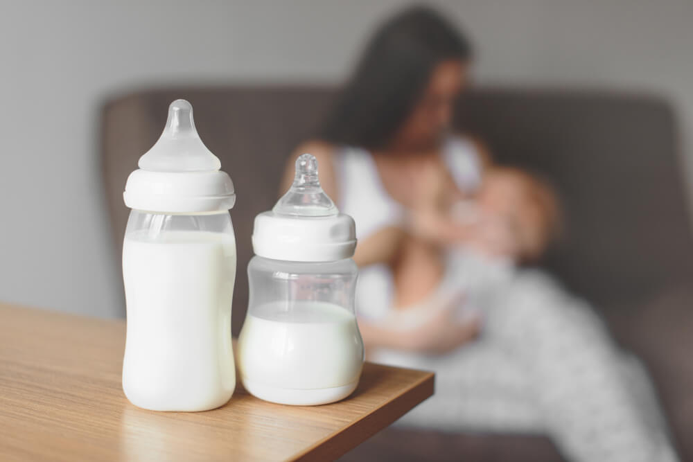 Two baby bottles with breastmilk in front of a mother breastfeeding her child