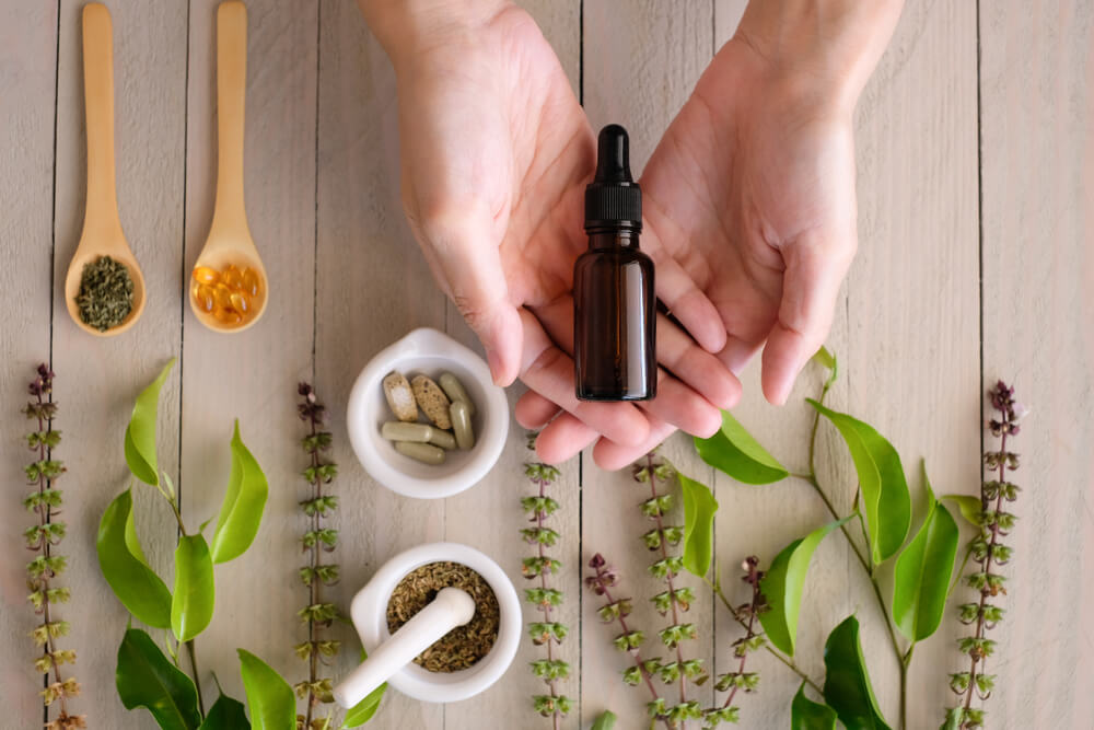Flat lay of person holding amber glass bottle next to botanicals and pills