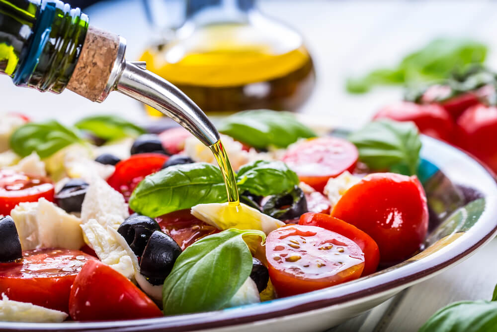 Olive oil being poured onto tomato, basil, and olive salad