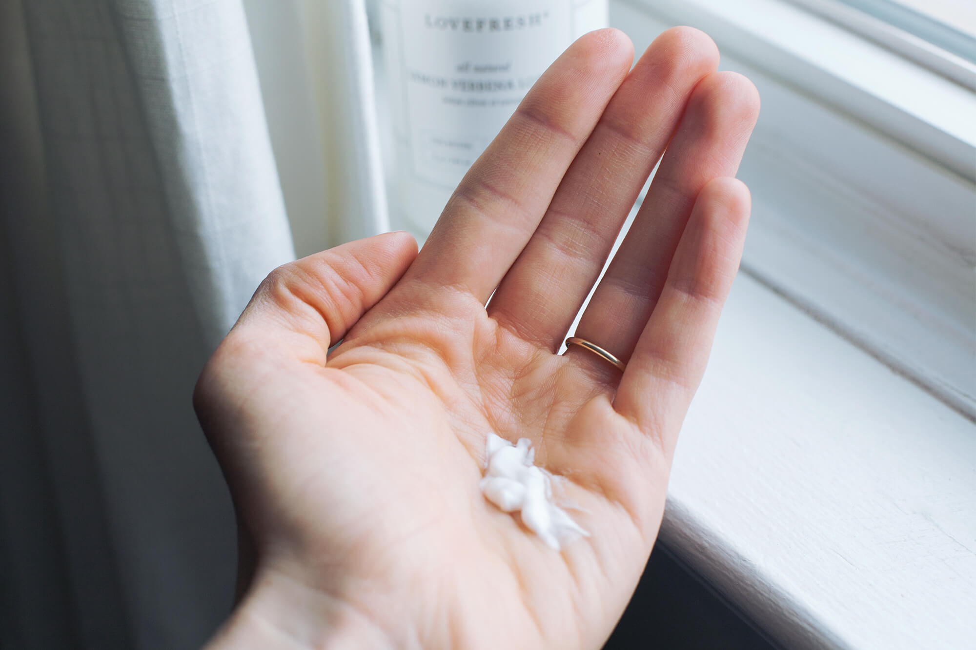 Hand cream in person's hand in front of a window
