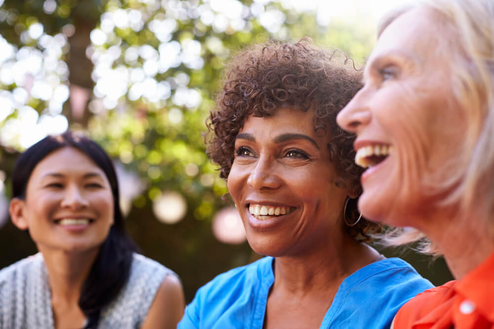 Three smiling women talk outside