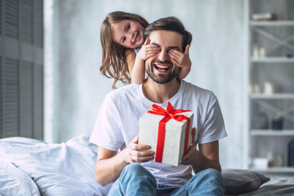 girl gives her dad a gift while holding his eyes closed