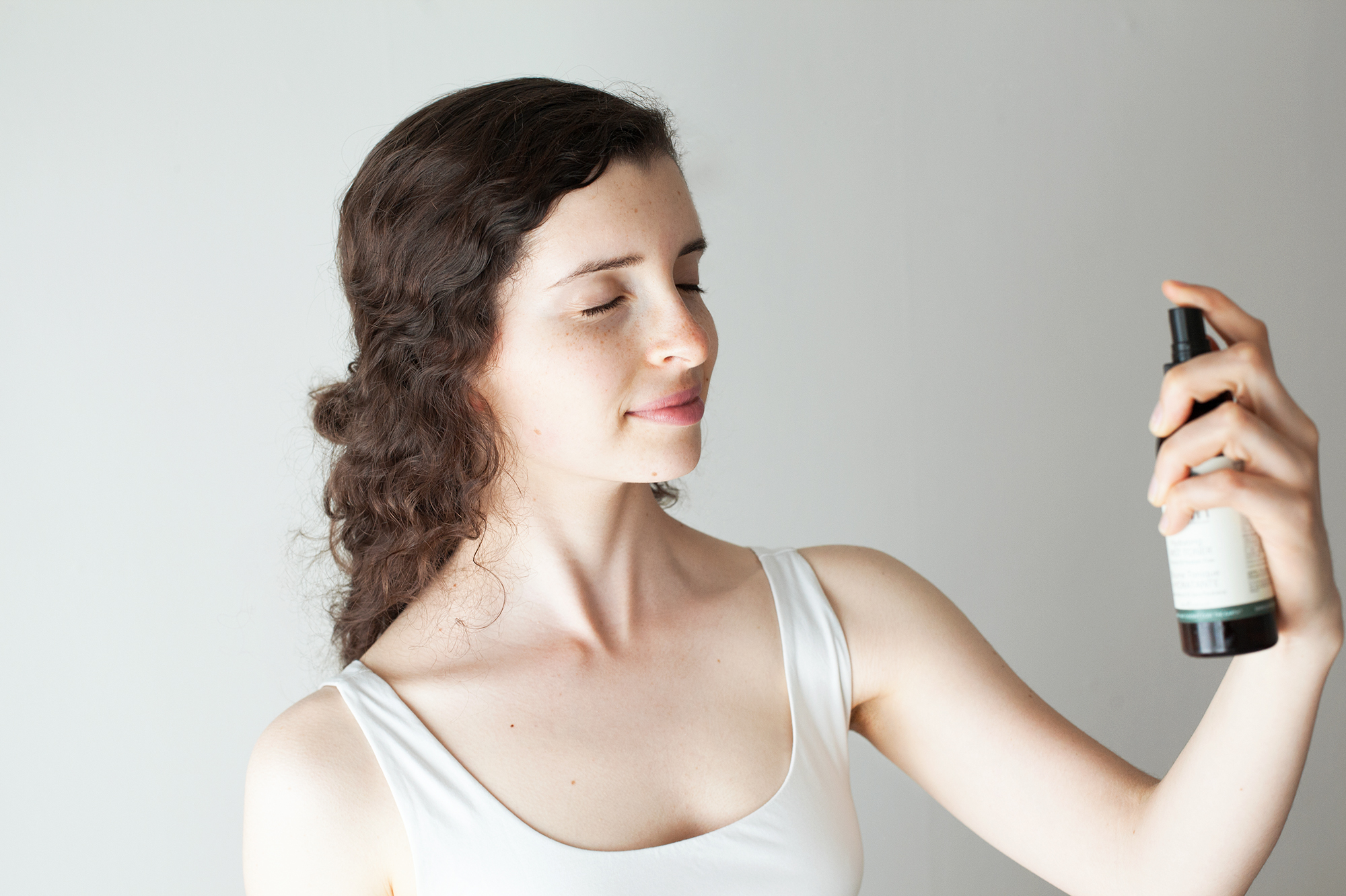 girl with dark hair spraying her face with mist