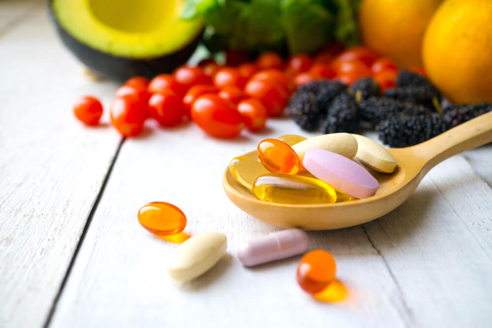 Vitamin supplements on a spoon with fruits and veggies in the background