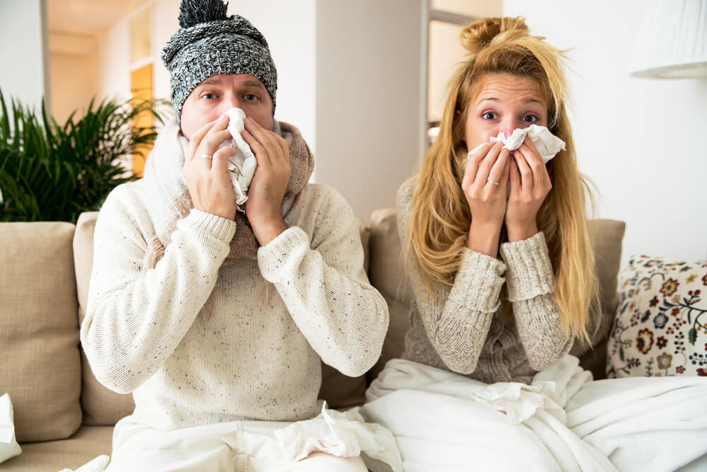 Man and woman sneezing while sitting on couch