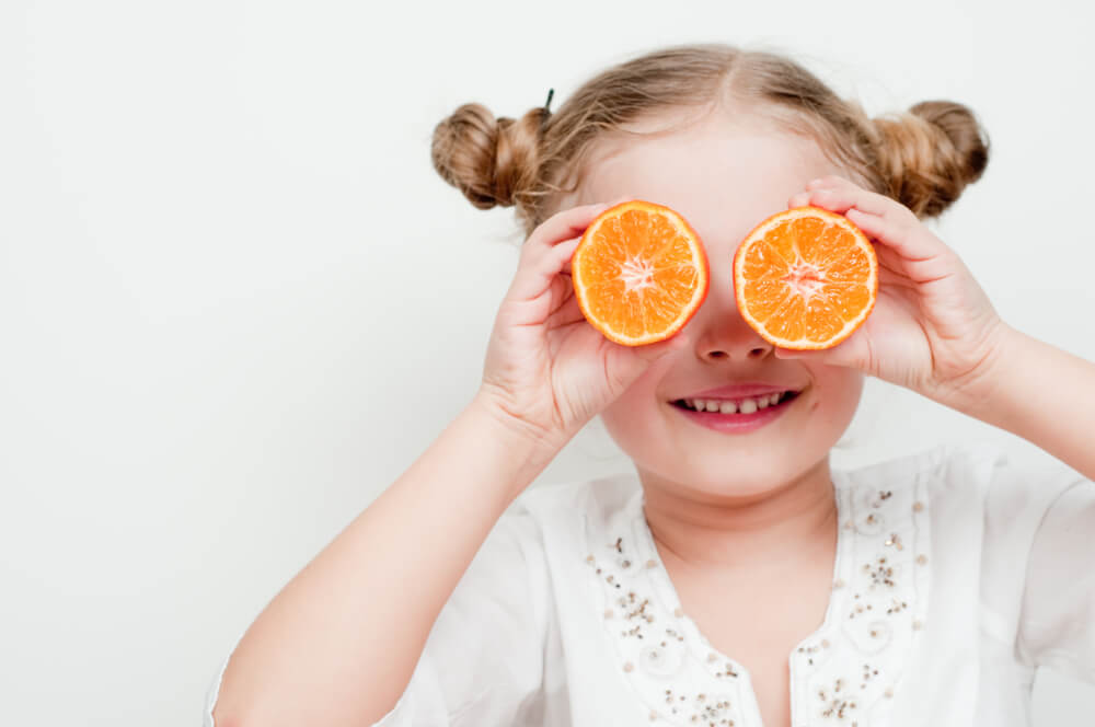 Young girl holding up orange slices to eyes