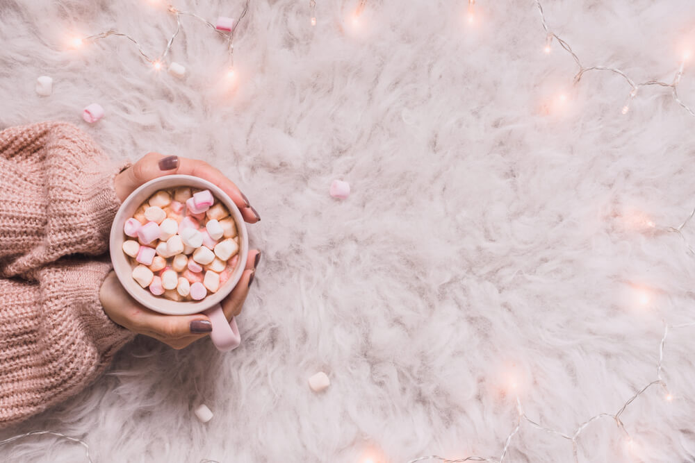 arms with pink sweater holding cup of hot cocoa
