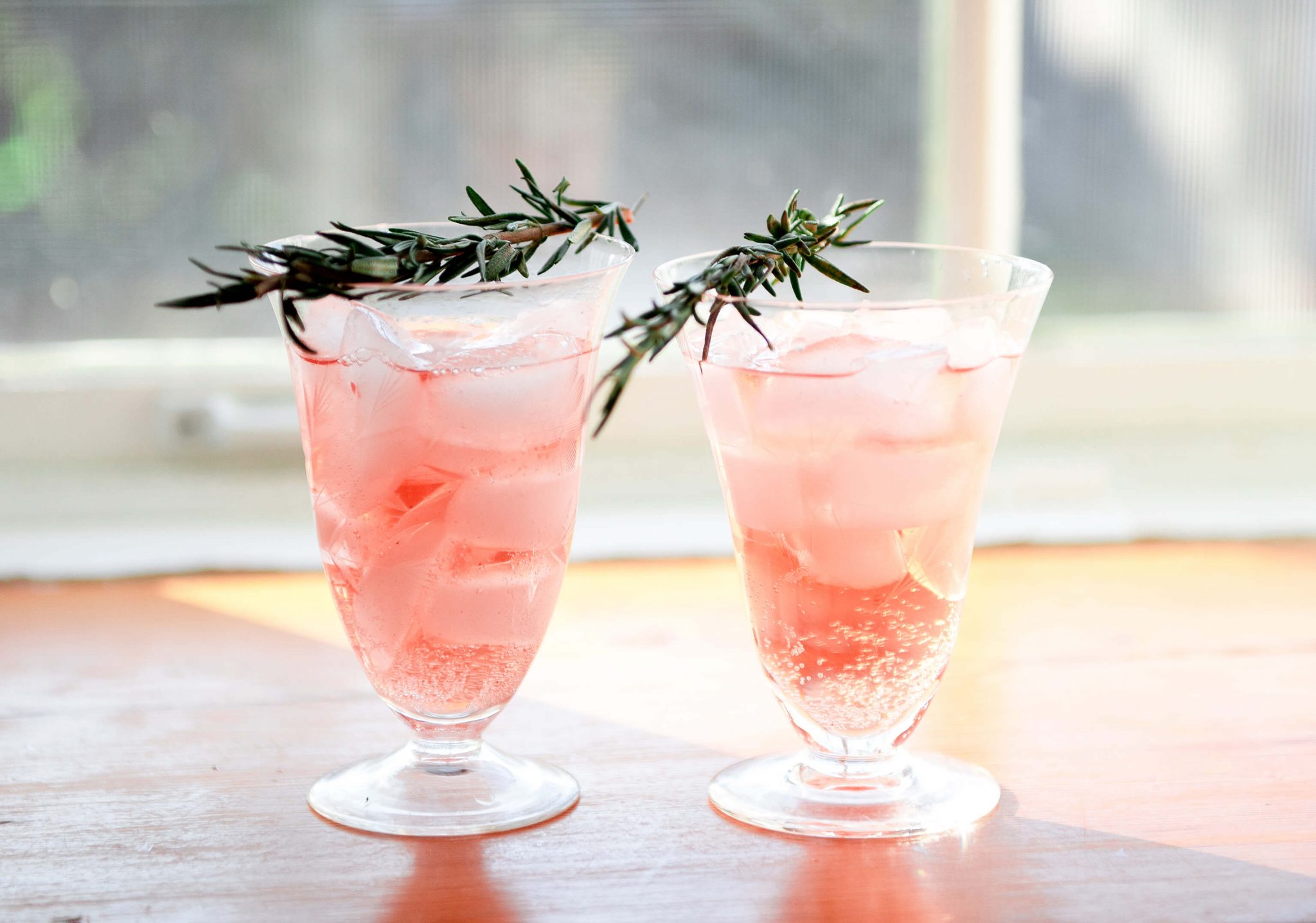 2 pink beverages garnished with rosemary