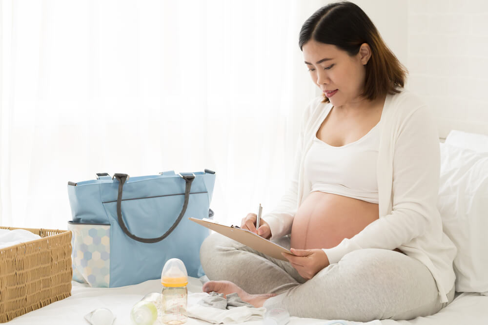 Pregnant woman sitting on bed packing bag for hospital