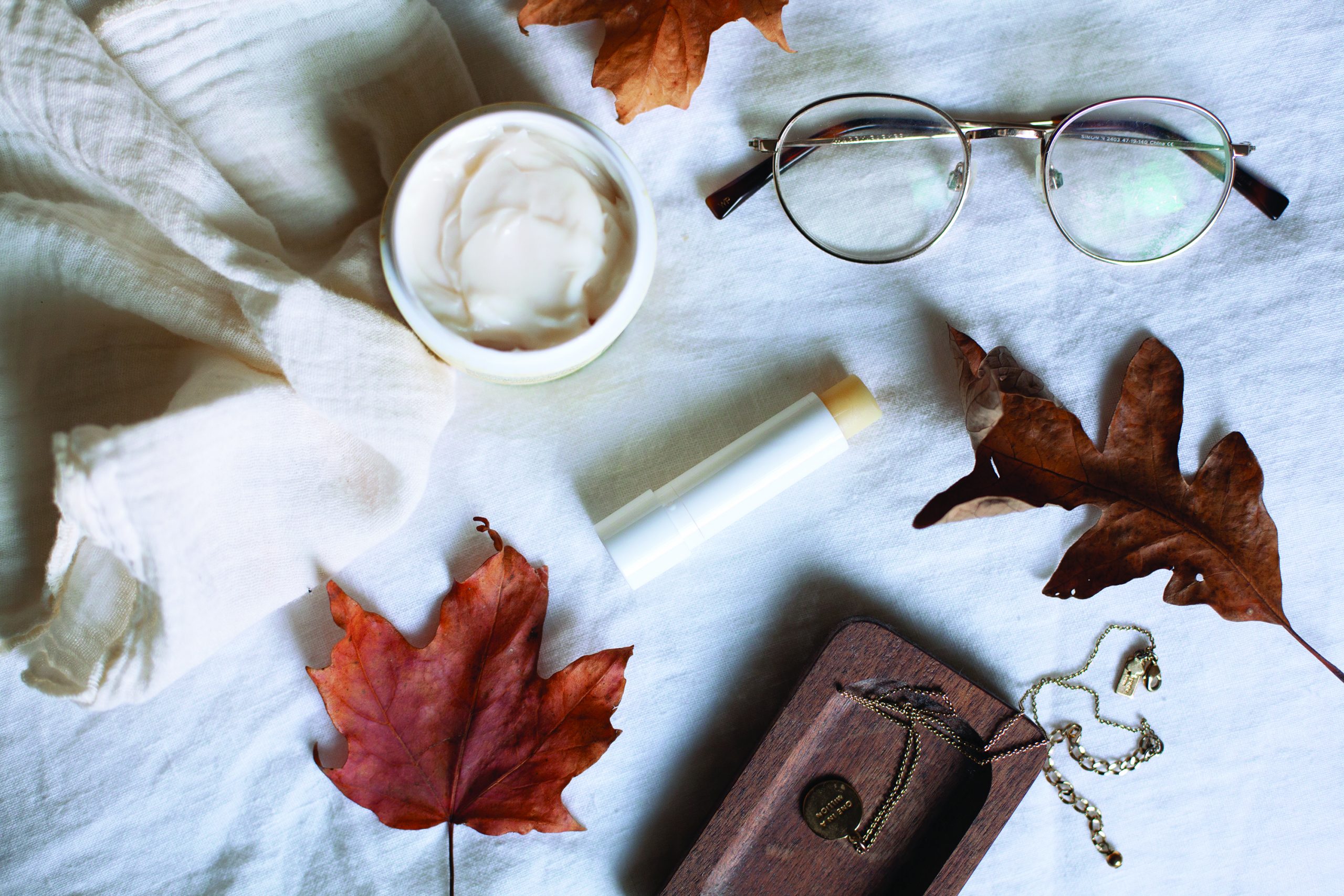 white background with leaves, hand cream and lip balm on it