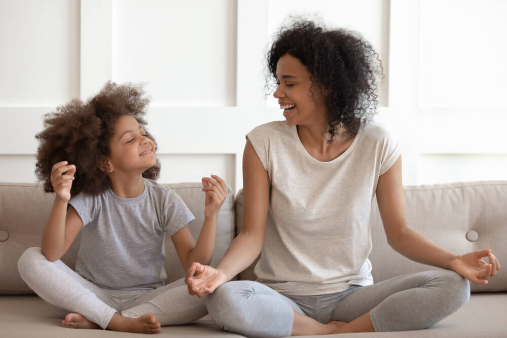 woman and daughter meditating on a couch