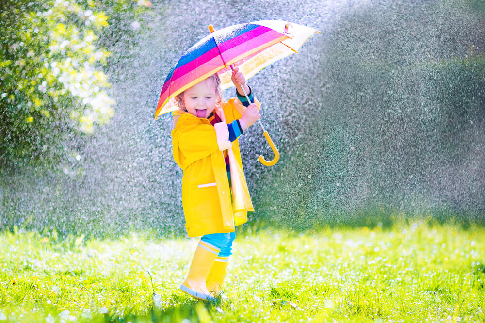 toddler playing the the rain with a rainbow umbrella