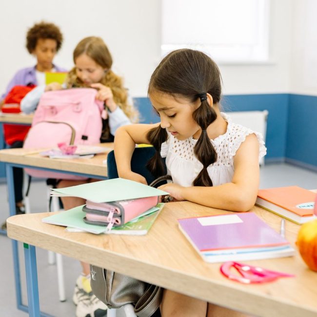 Girl sitting at school desk with notebook, water bottle and apple