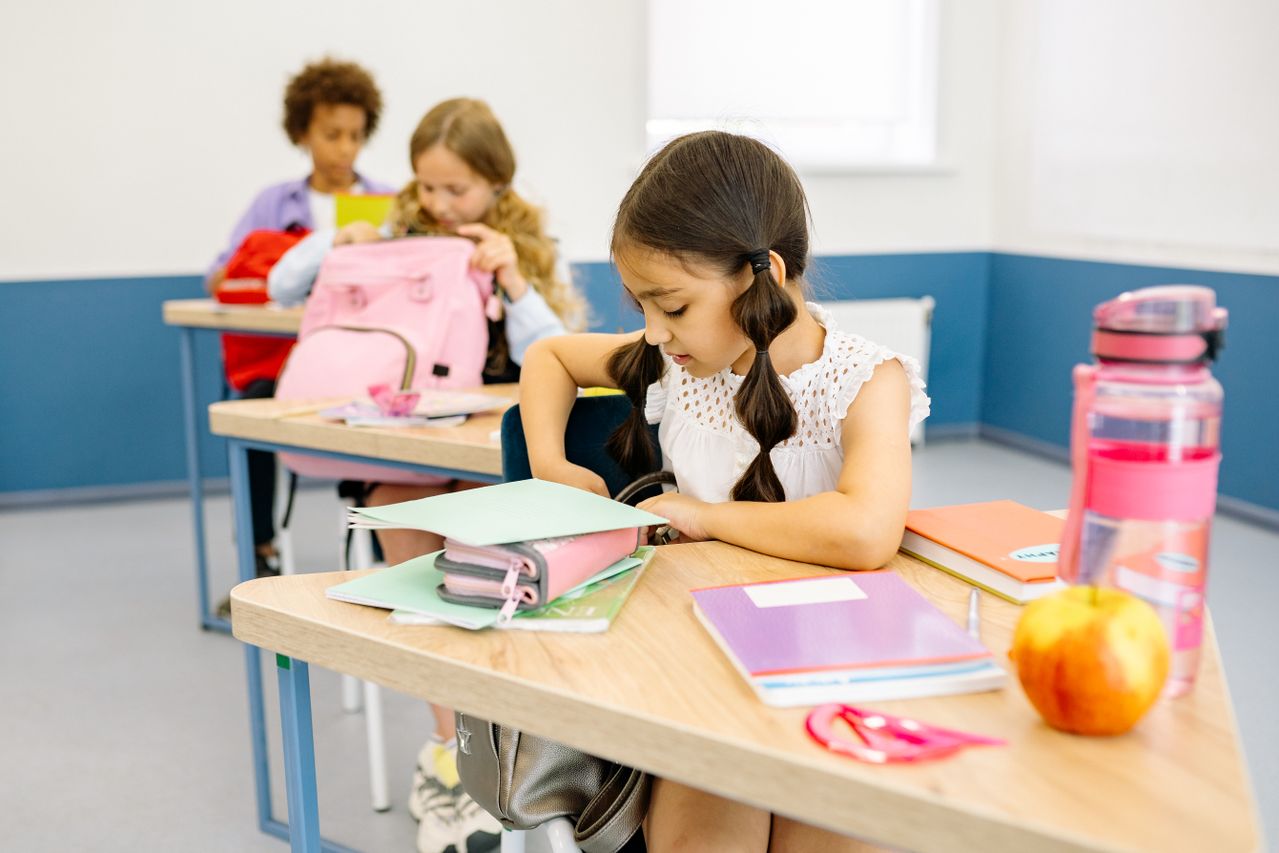 Girl sitting at school desk with notebook, water bottle and apple